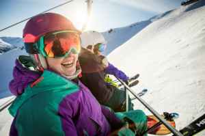 A group of friends sit on a chairlift in the sun.