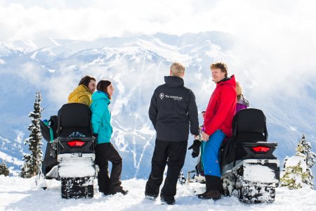 A group of people rest at the top of Whistler on snowmobiles.