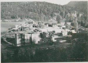 a vintage photo of a boat and mill, Parkhurst Ghosttown next to a body of water